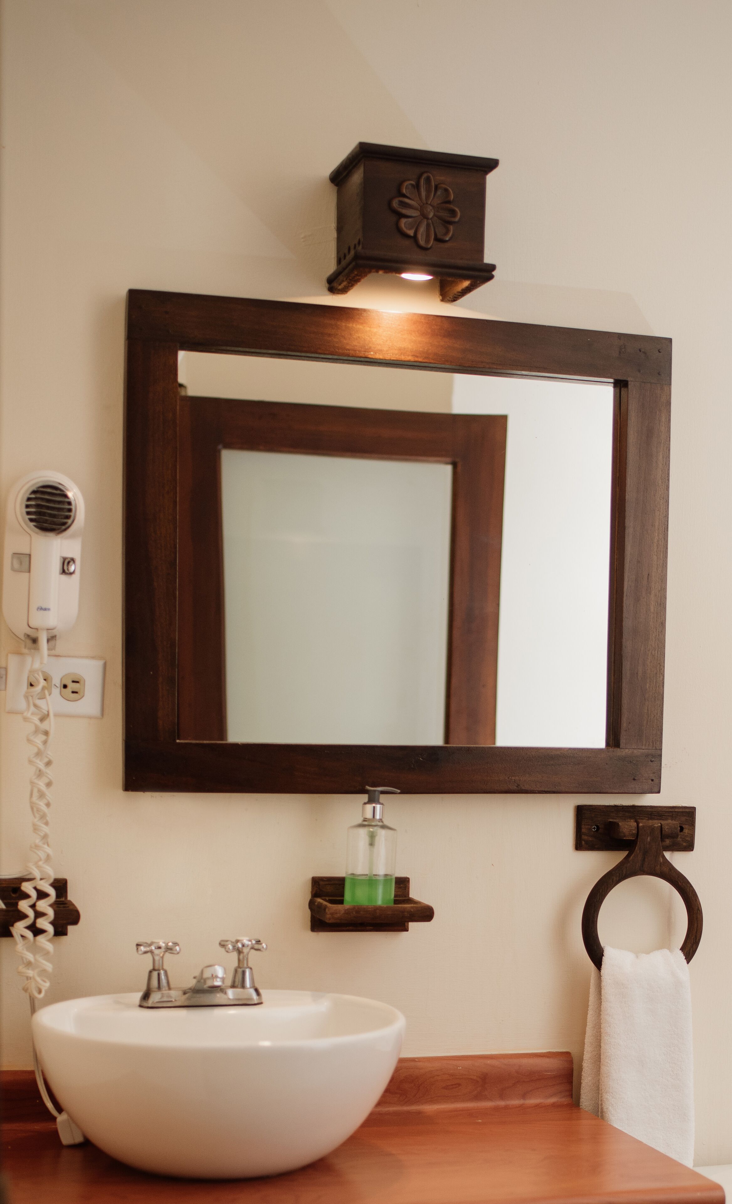 A bathroom with a white sink, a mirror, a hairdryer, a soap dispenser, and a towel ring.