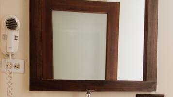 A bathroom with a white sink, a mirror, a hairdryer, a soap dispenser, and a towel ring.