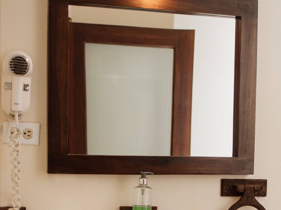 A bathroom with a white sink, a mirror, a hairdryer, a soap dispenser, and a towel ring.