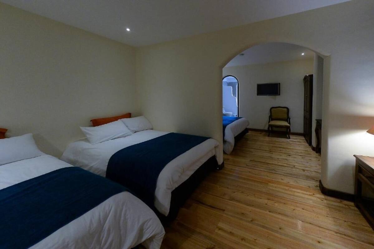 Habitación de hotel con dos camas, suelo de madera, televisión y una pequeña zona de estar.