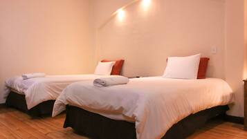 Two single beds with white linens and orange pillows, wooden flooring, and a curved wall with built-in lighting.