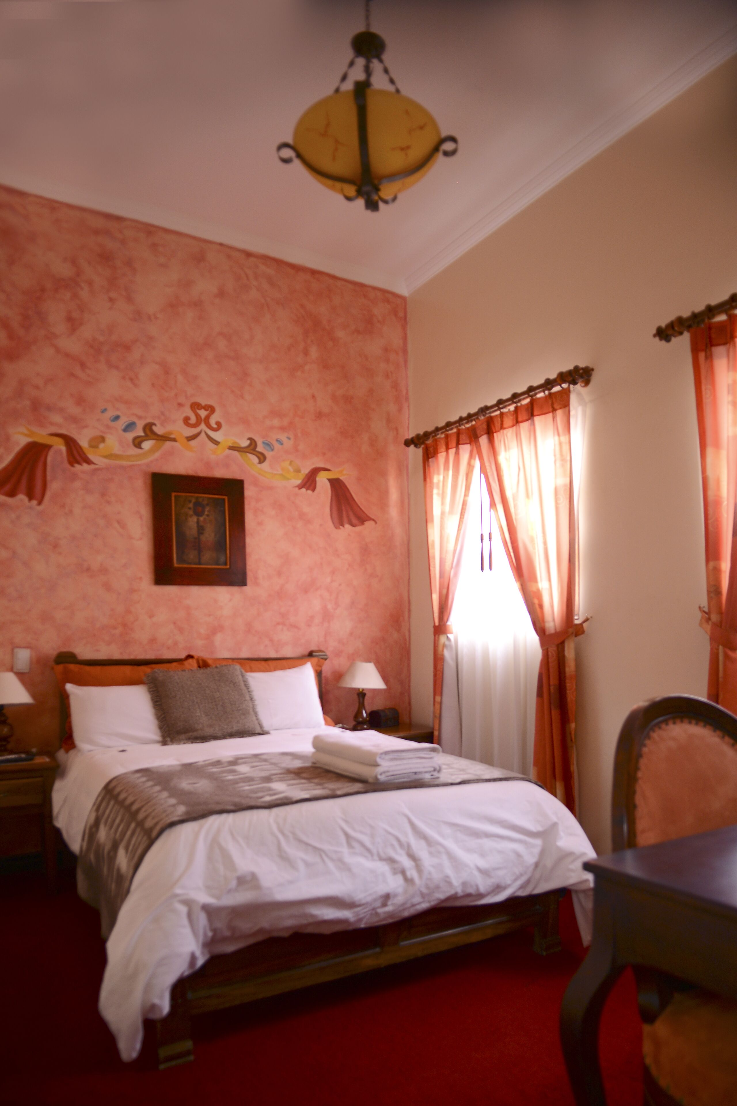 Un dormitorio con cama de madera, dos mesitas de noche con lámparas, un adorno en la pared y una ventana con cortinas.