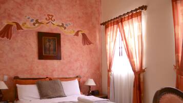 Un dormitorio con cama de madera, dos mesitas de noche con lámparas, un adorno en la pared y una ventana con cortinas.