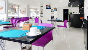 A modern dining area with purple and black tables and chairs, a reception desk, and a kitchen area.