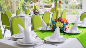 A dining area with green chairs and white table settings, including plates, napkins, and a centerpiece with flowers.