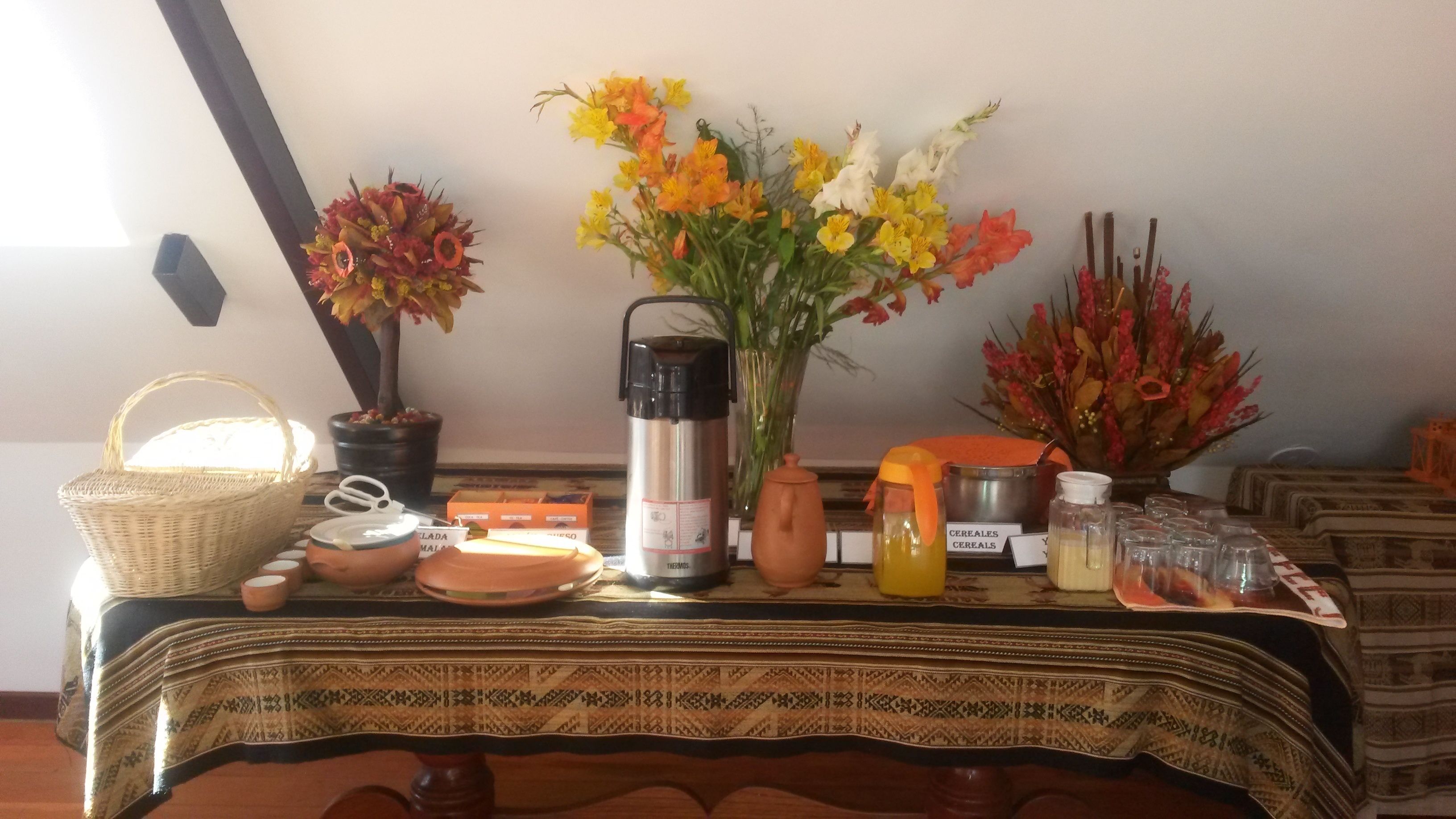 A table with a thermos, a basket, a vase with flowers, a pitcher, and a bottle of juice.