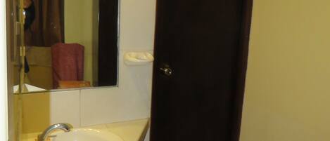A bathroom with a white sink, a mirror, and a dark wooden door.