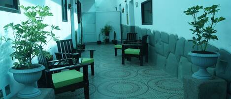 A spacious indoor area with a patterned floor, several chairs with green cushions, and potted plants.