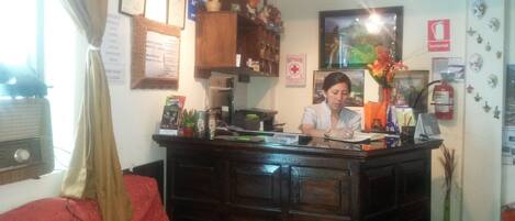 A reception desk with a woman behind it, a wooden counter, a red sofa, and a wall with various items and a fire extinguisher.