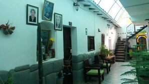 Un pasillo estrecho con una escalera, cuadros en las paredes y plantas en macetas.