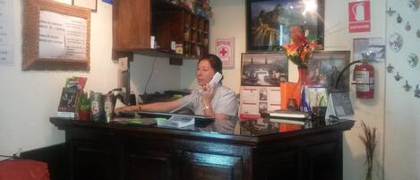 A reception desk with a receptionist, framed certificates, a fire extinguisher, and a calendar on the wall.