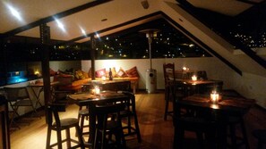 Un comedor interior con mesas y sillas, un sofá y vista al cielo nocturno.