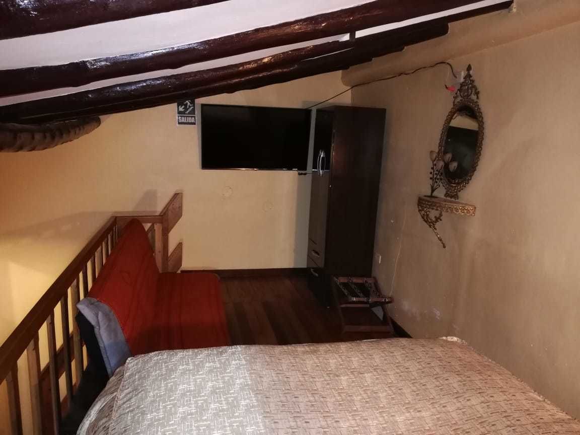 A bedroom with a bed, a wooden staircase, a wardrobe, and a television.