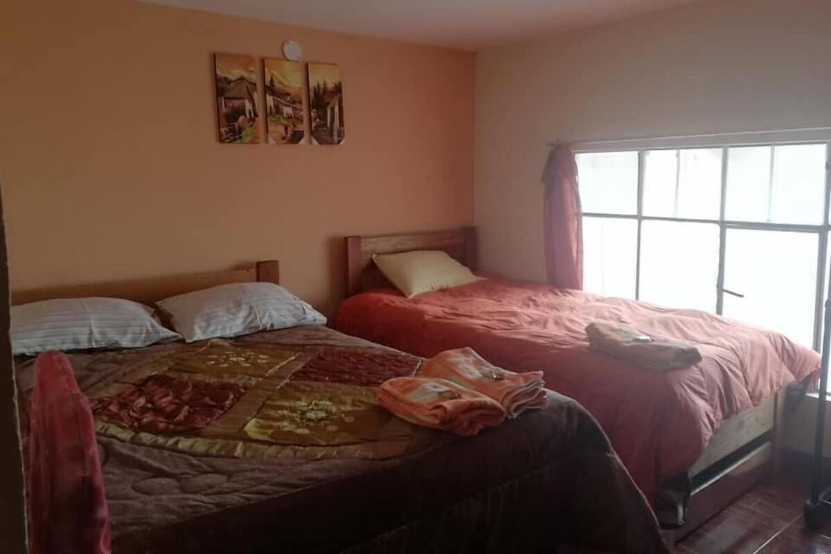 Un dormitorio con dos camas, una ventana con cortinas y tres cuadros colgados en la pared.