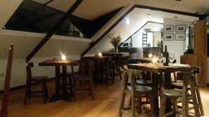 A dining area with wooden tables and chairs, a staircase, and a kitchen in the background.