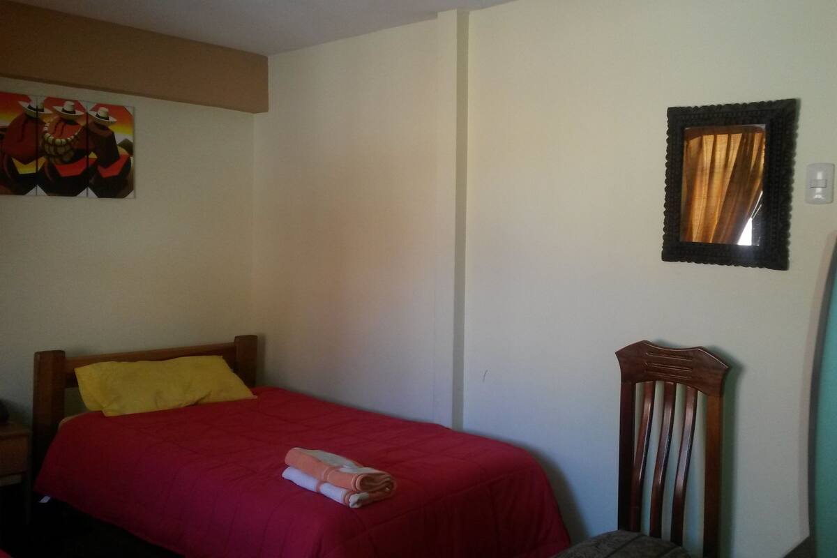 Una habitación con una cama, una silla, un espejo y una pared decorada con un cuadro.