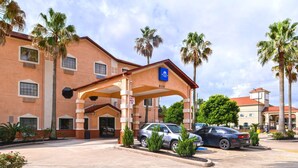 L’entrée d’un hôtel avec un espace de stationnement couvert, des palmiers et un ciel dégagé.