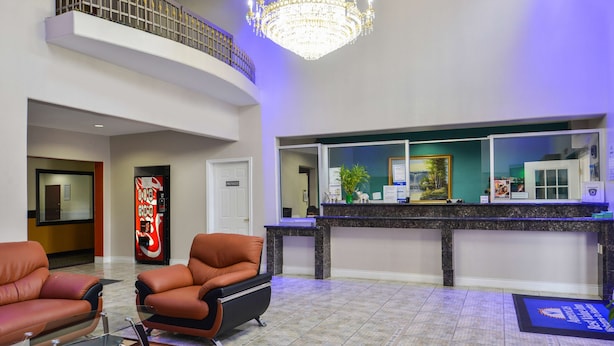 Un hall d’hôtel avec des fauteuils en cuir, un comptoir d’accueil, un lustre et une porte privative.