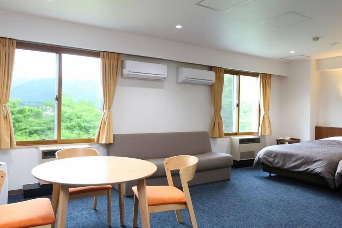 Habitación de hotel con cama, sofá, una mesa redonda con sillas y dos unidades de aire acondicionado en la pared.