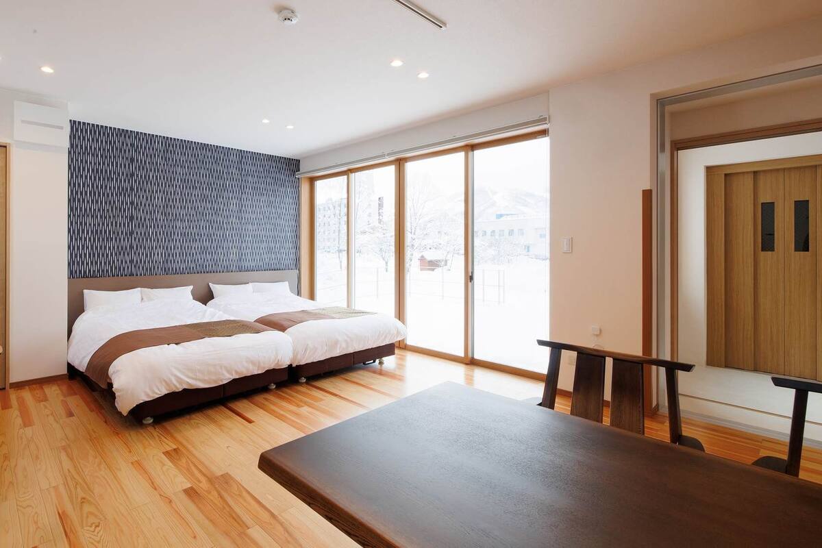 Un dormitorio moderno con una cama grande, suelo de madera, un escritorio y una puerta corrediza de vidrio a un balcón.