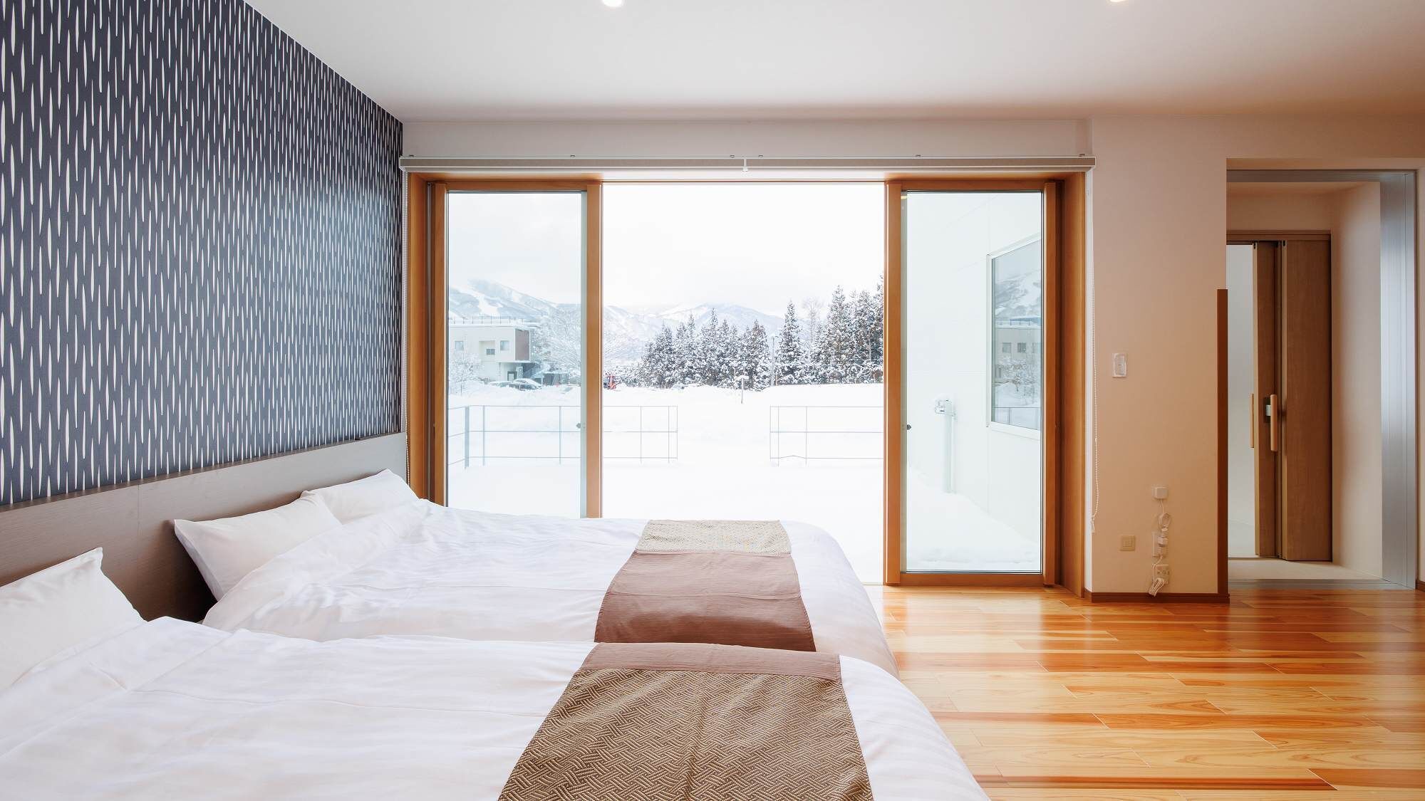 Quarto de hotel com cama, uma janela grande e vista para árvores cobertas de neve.