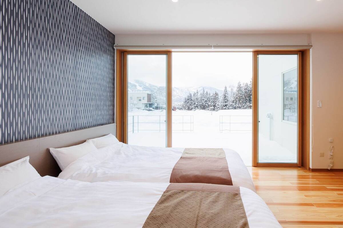 Habitación de hotel con cama, un ventanal y vistas a árboles cubiertos de nieve.