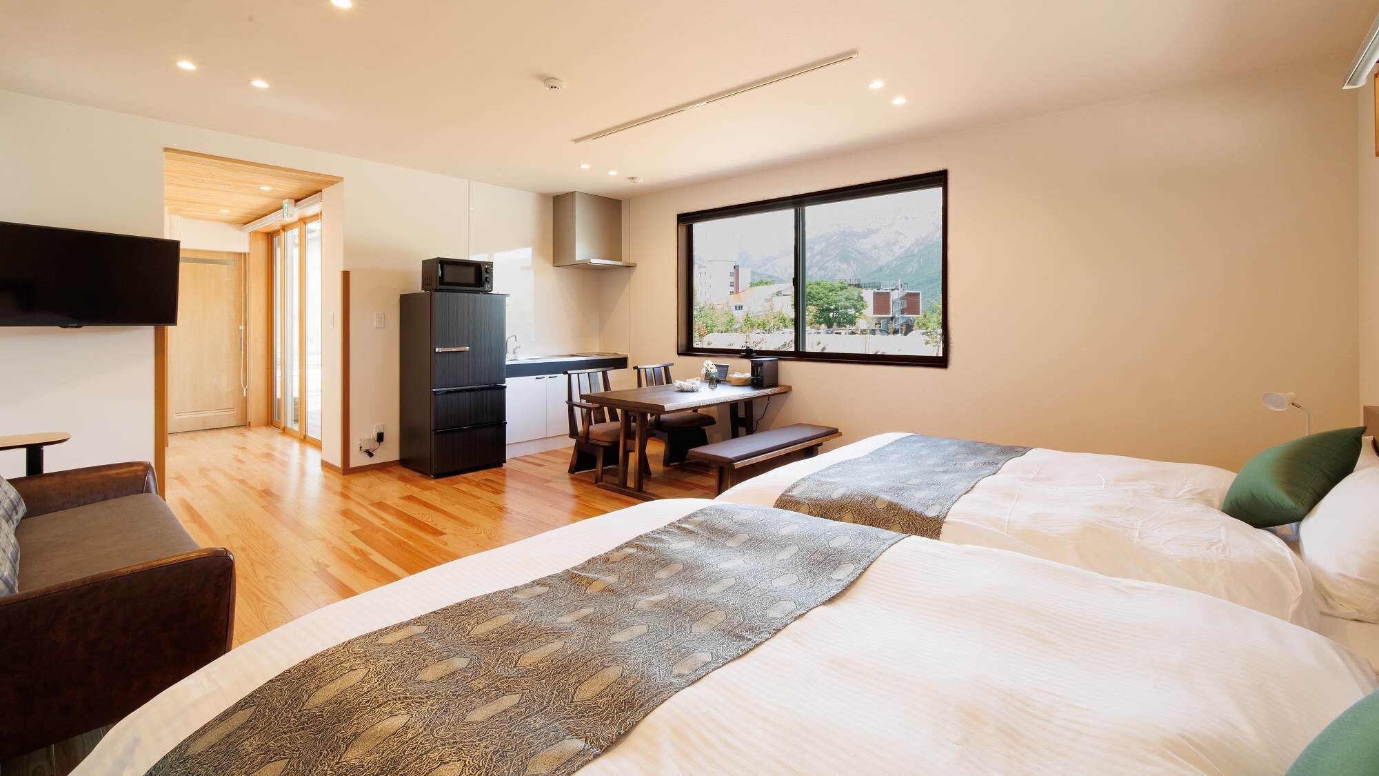 Quarto de hotel com duas camas, área de refeições, cozinha e televisão.