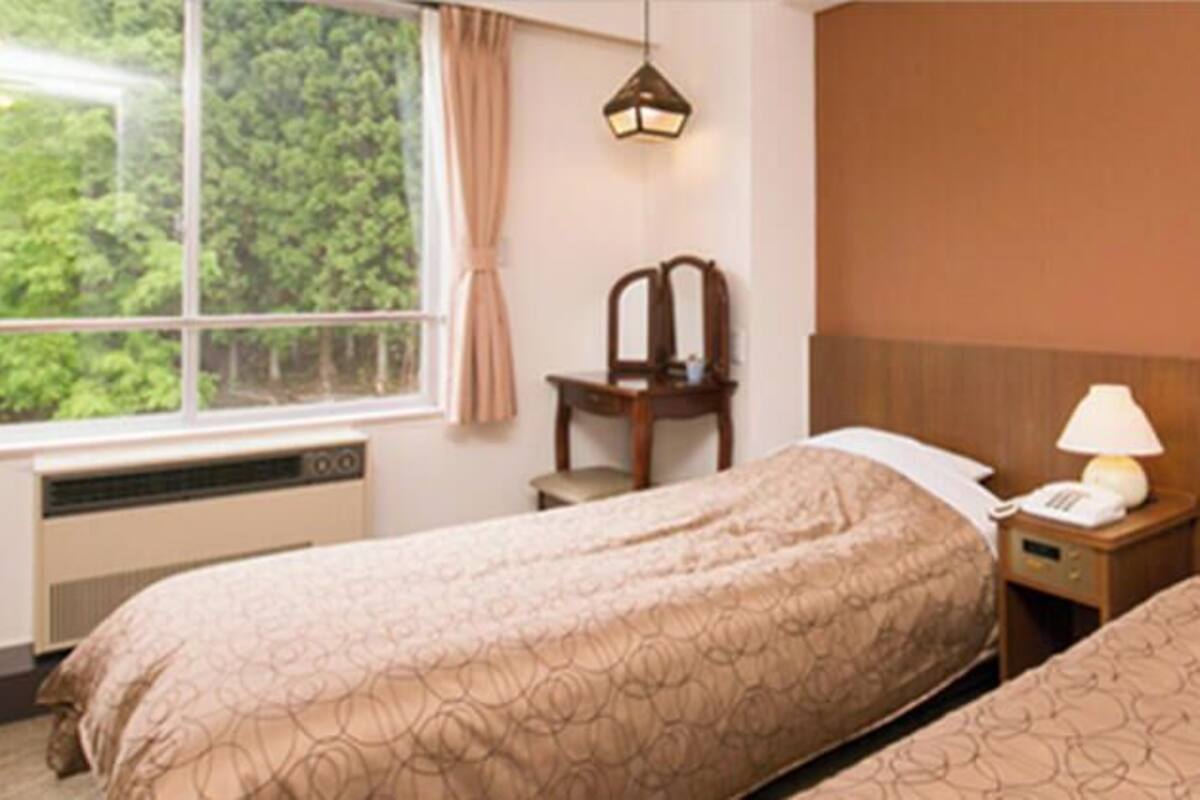 Habitación de hotel con dos camas, una ventana con cortinas, un escritorio con lámpara y un calentador.