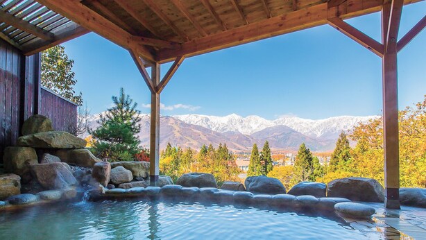 A hot spring area with a wooden pergola, rocks, and a mountain view. - Hakuba Highland Hotel (Hakuba)
