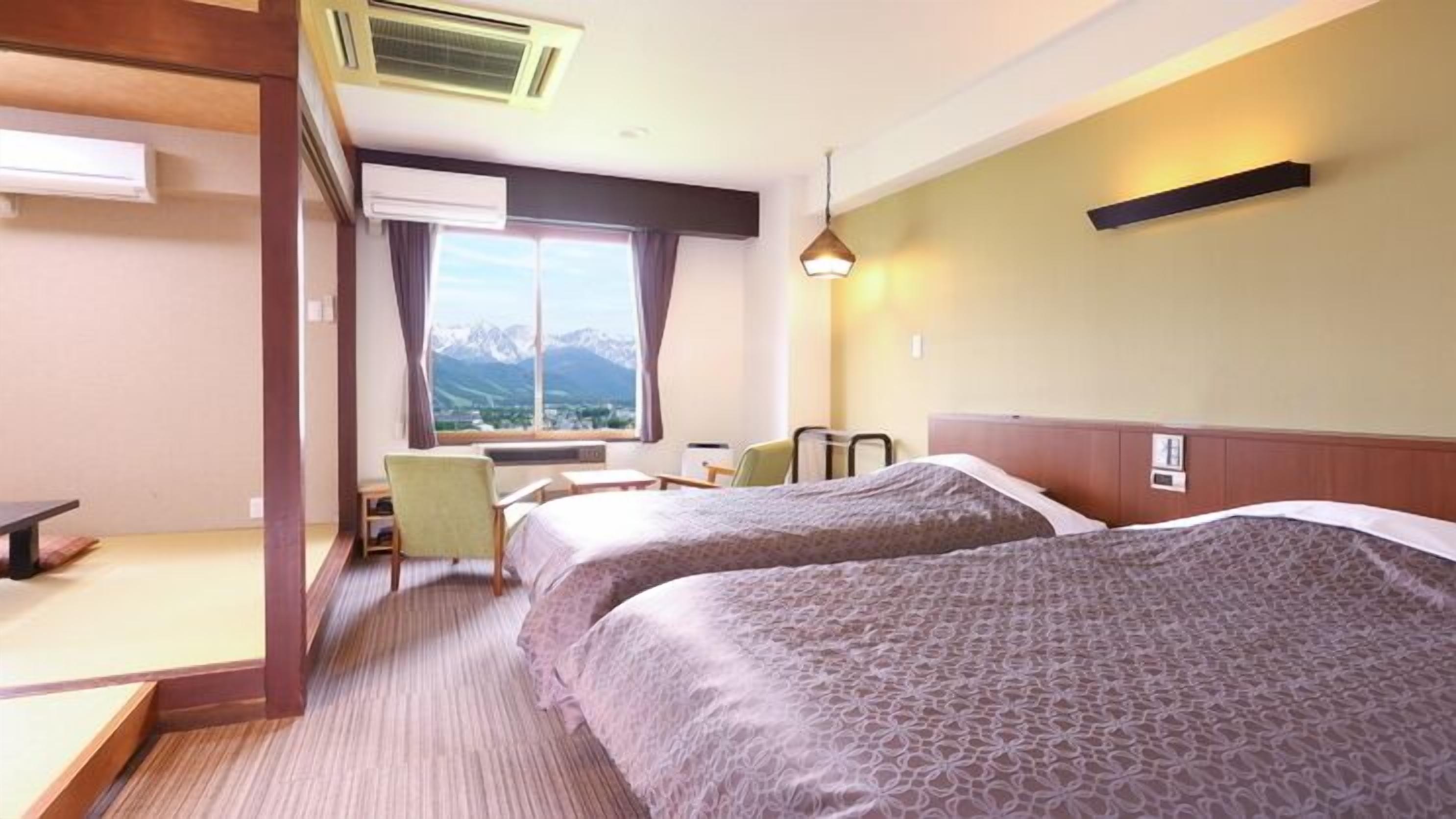 Quarto de hotel com duas camas, uma escrivaninha, uma cadeira e uma janela com vista para as montanhas.