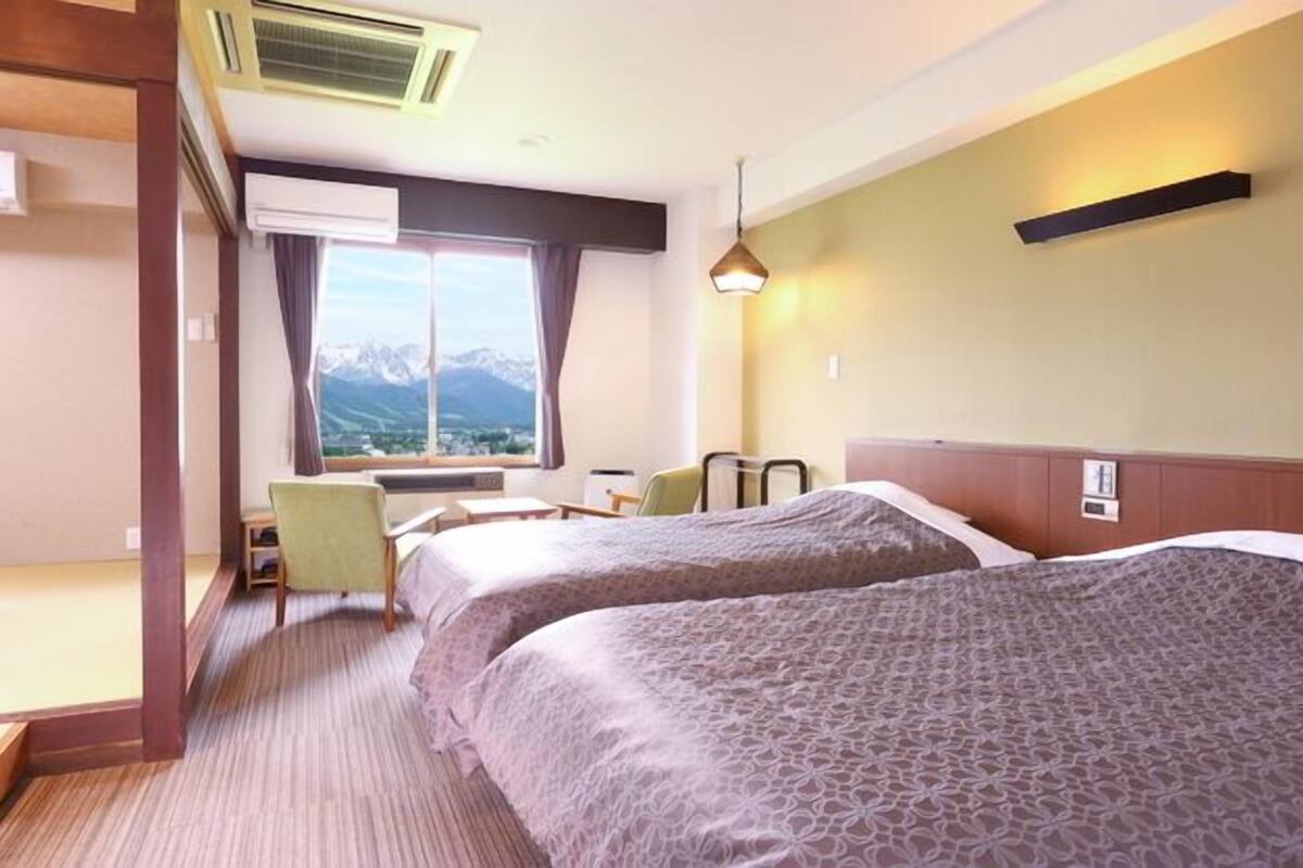 Habitación de hotel con dos camas, un escritorio, una silla y una ventana con vista a las montañas.