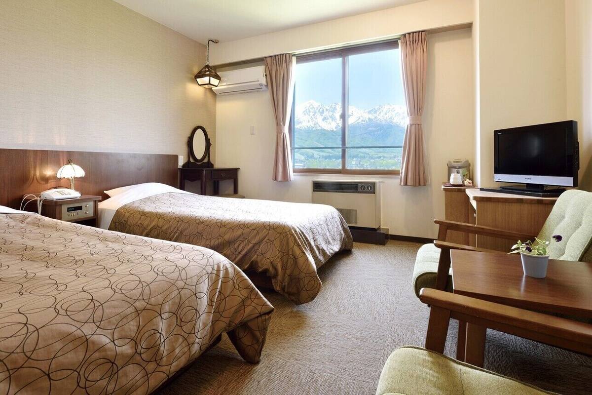 Habitación de hotel con dos camas, televisión, escritorio y vistas a montañas.