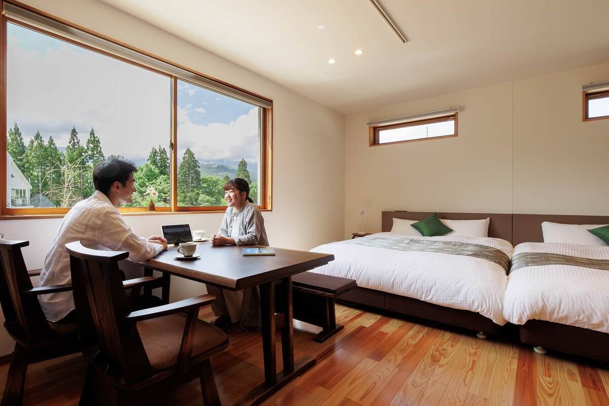 Una habitación con un ventanal grande, una cama, un escritorio y dos sillas.