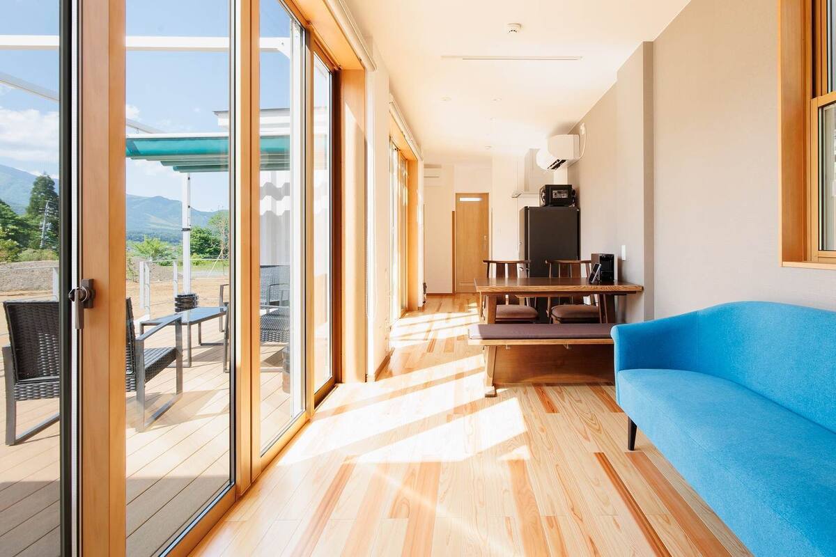 Un interior moderno con piso de madera, un sofá azul y una zona de comedor con mesa y sillas.