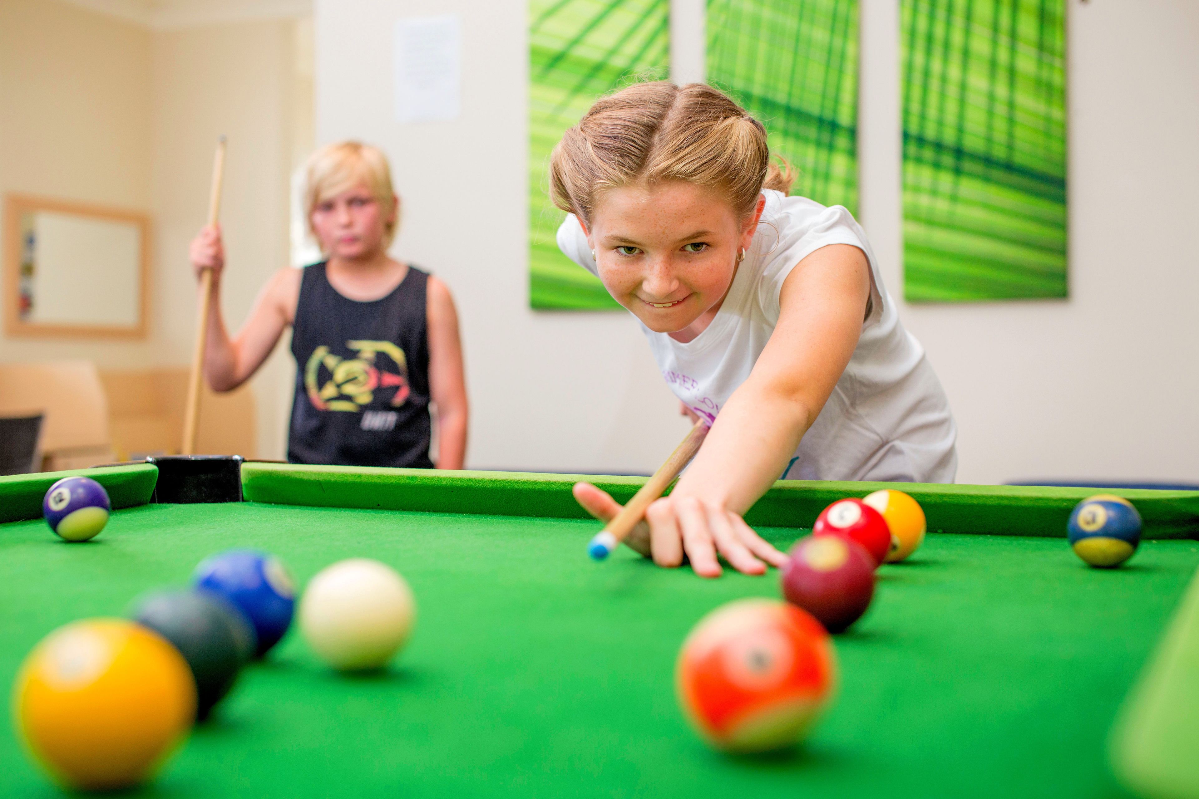 A pool table with balls and a child leaning over it.