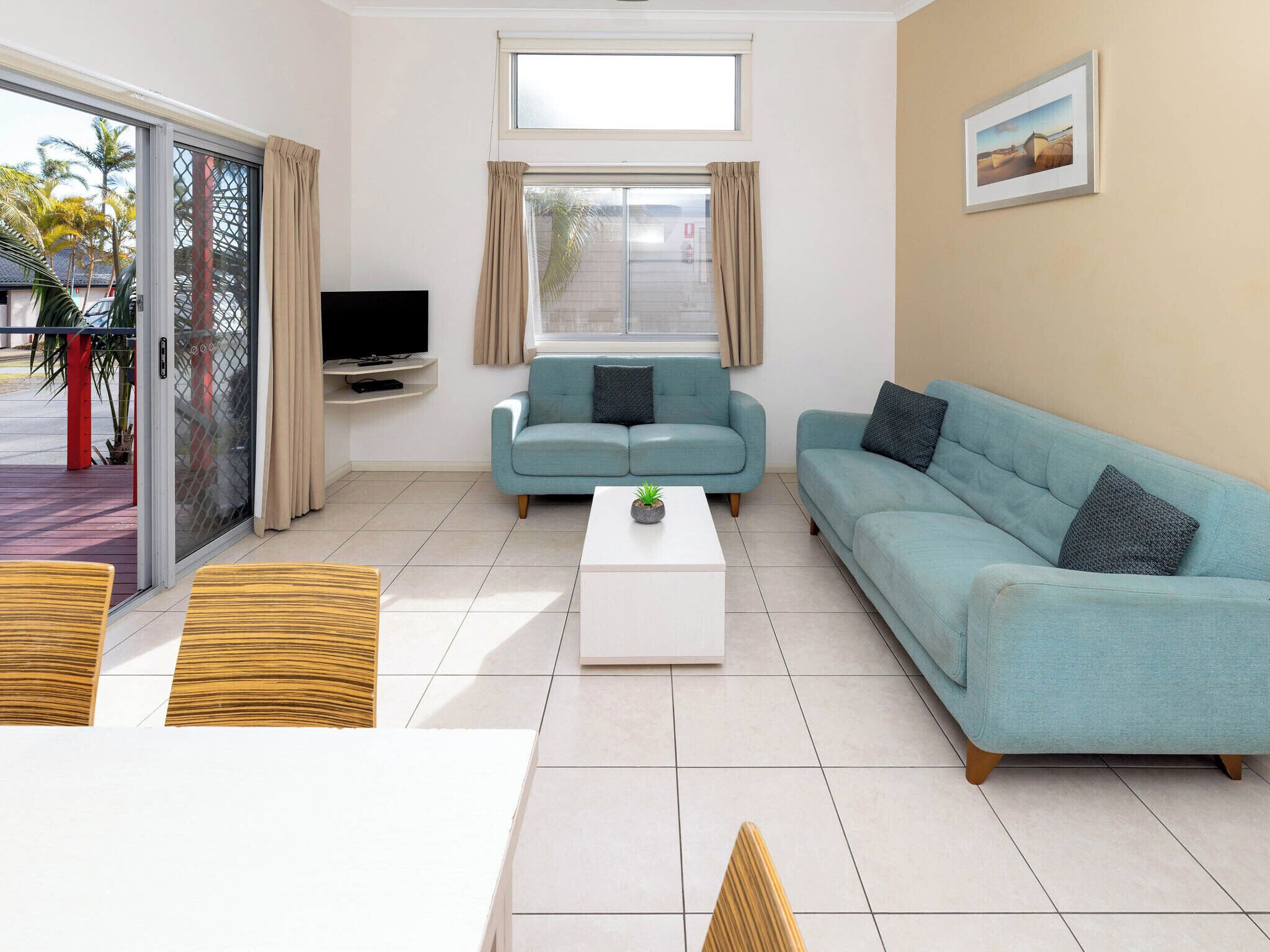 Una sala de estar con un sofá, una mesa de centro, un televisor y un ventanal corredizo que da a un espacio exterior.