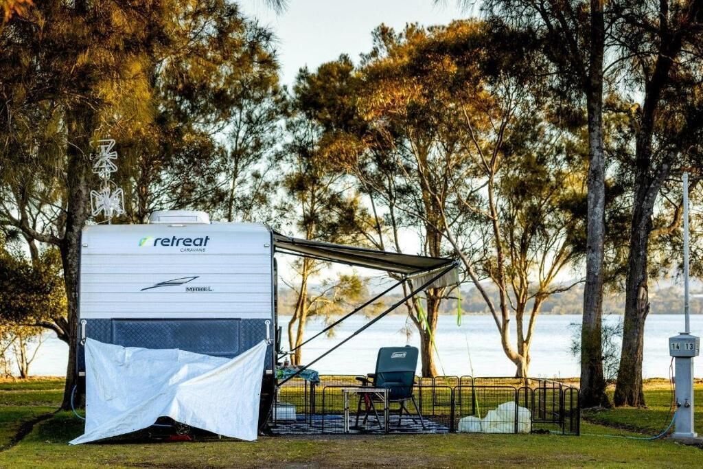 A retreat caravan with a covered seating area, a chair, and a view of a lake.