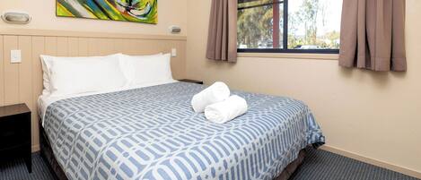 A hotel room with a bed, a painting on the wall, and a window with curtains.