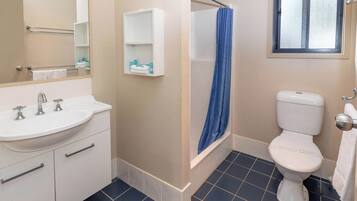 A bathroom with a white sink, two faucets, a mirror, a white toilet, a blue shower curtain, and a window with frosted glass.