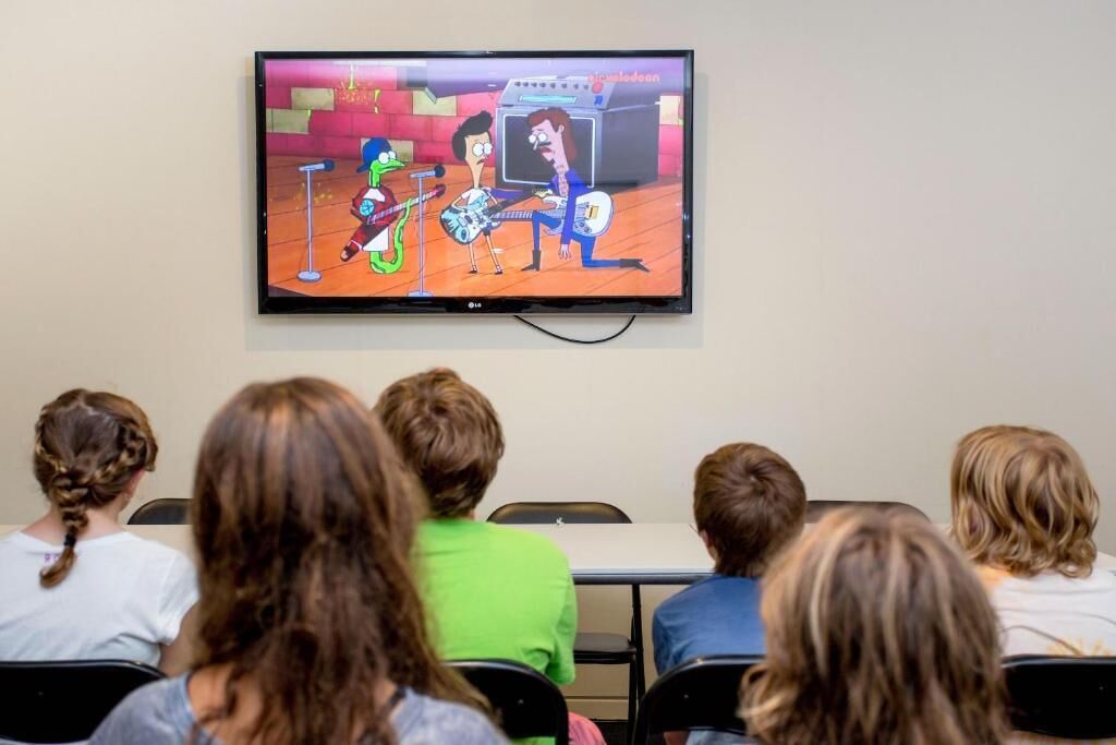 A television displaying an animated show in a room with people seated facing it.