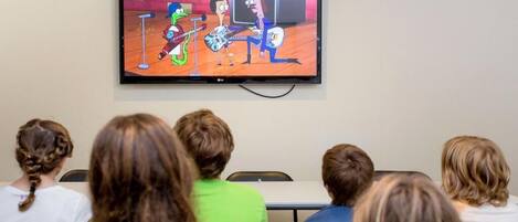 A television displaying an animated show in a room with people seated facing it.
