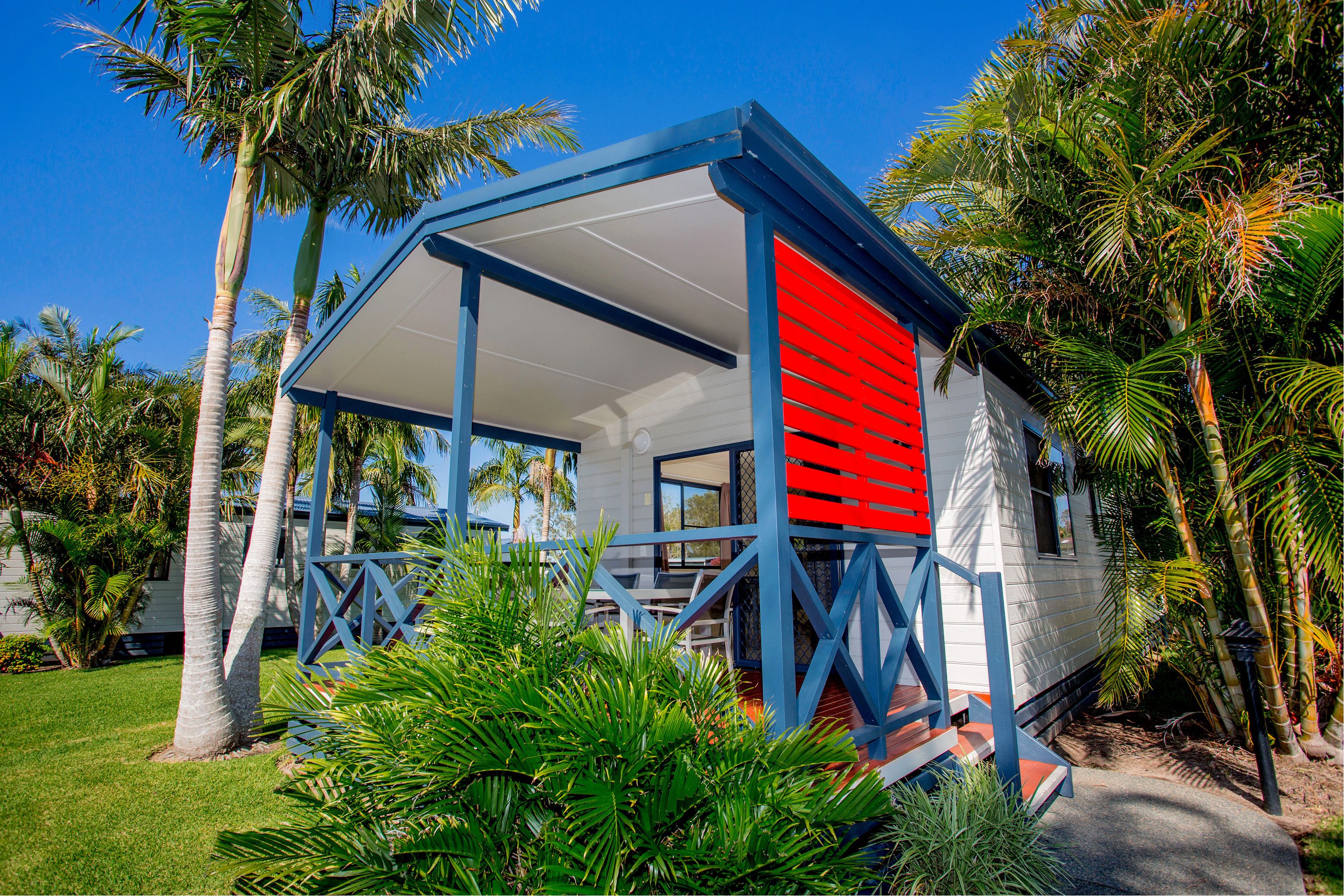 A small, single-story house with a blue and white exterior, surrounded by lush greenery and palm trees.