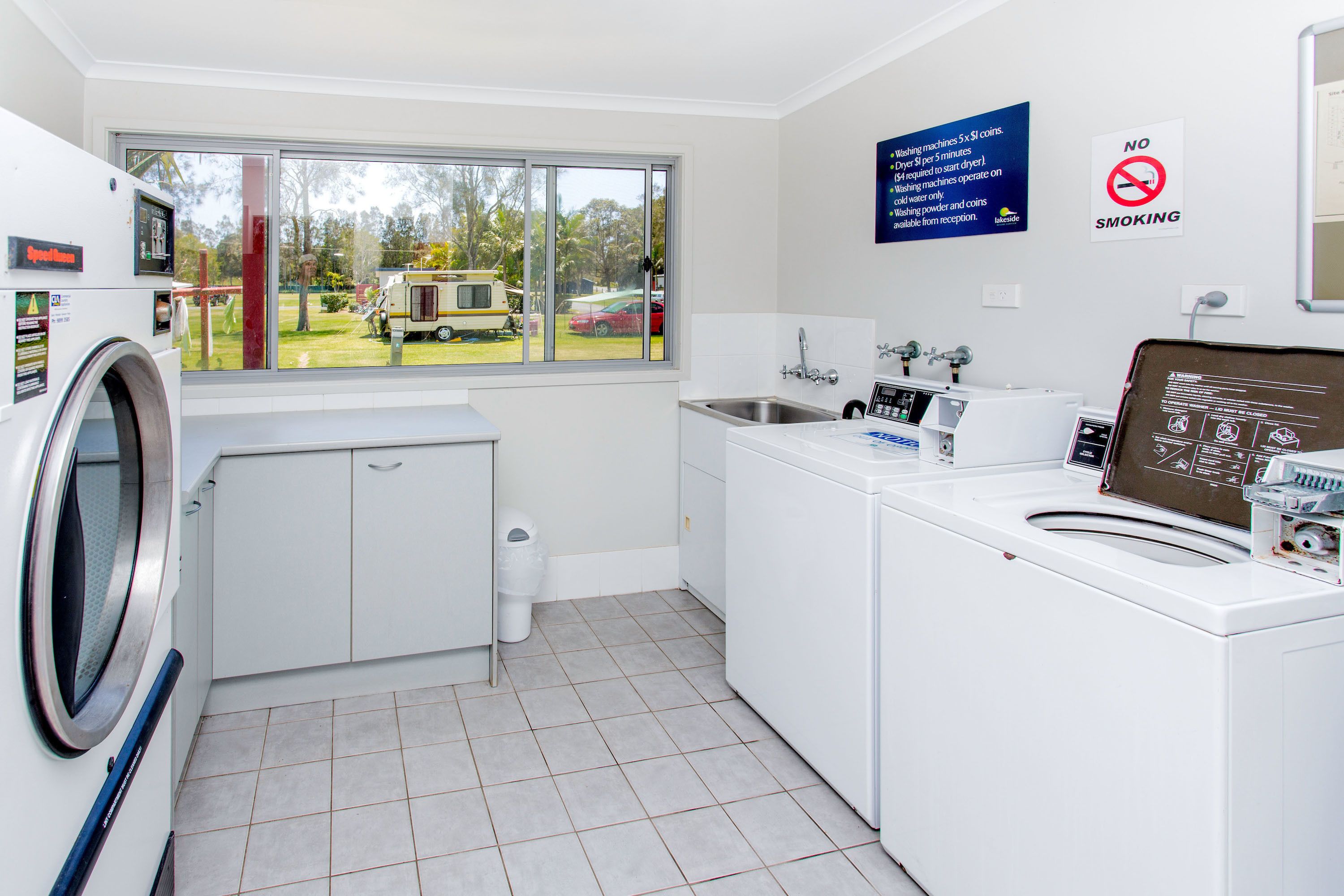 A laundry room with a washing machine, dryer, and sink. There is a window with a view of a vehicle outside.