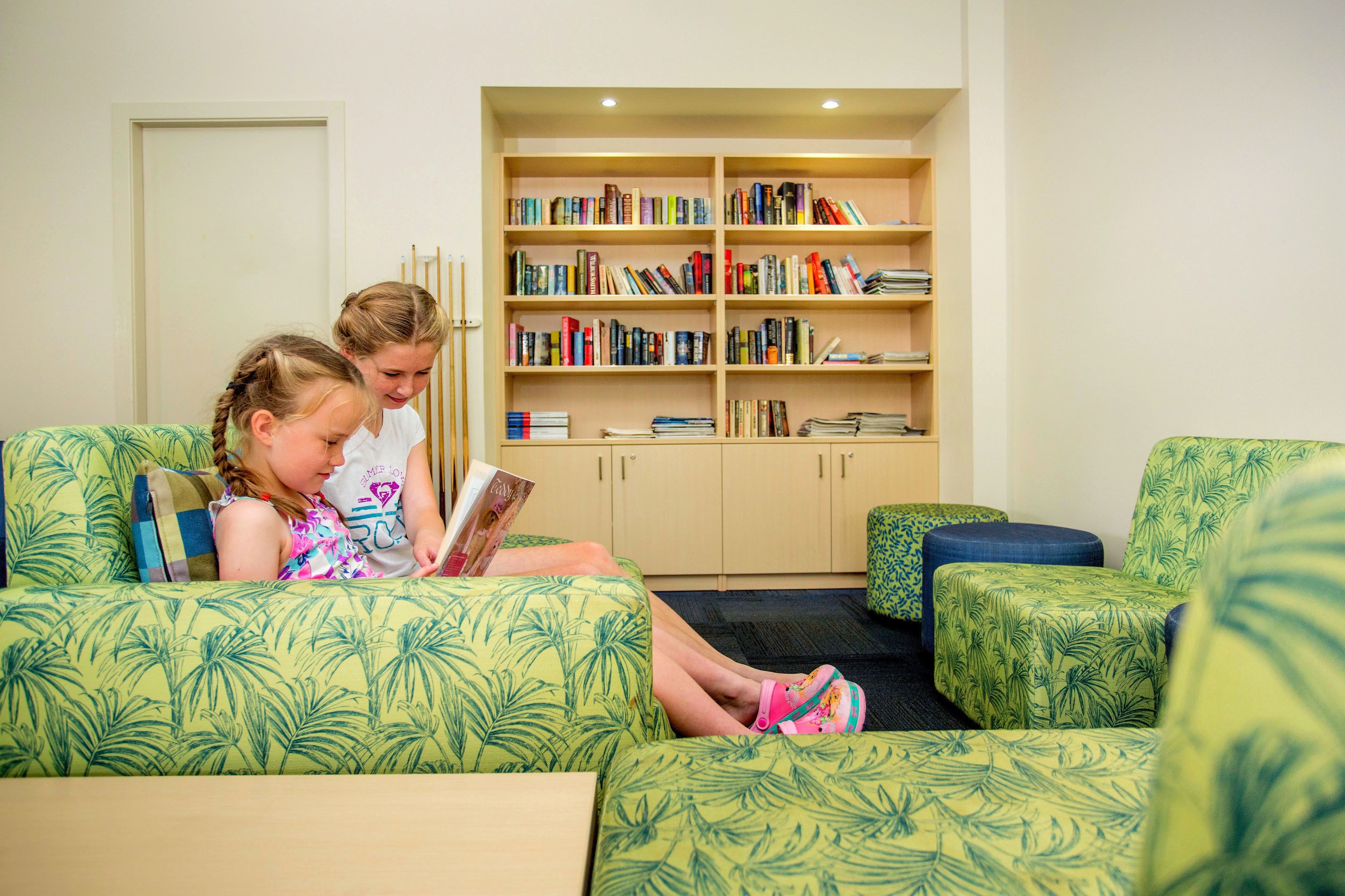 A room with a green patterned sofa, a bookshelf, and a door.