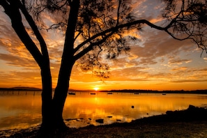 A sunset over a calm lake with silhouettes of trees and a distant shoreline.