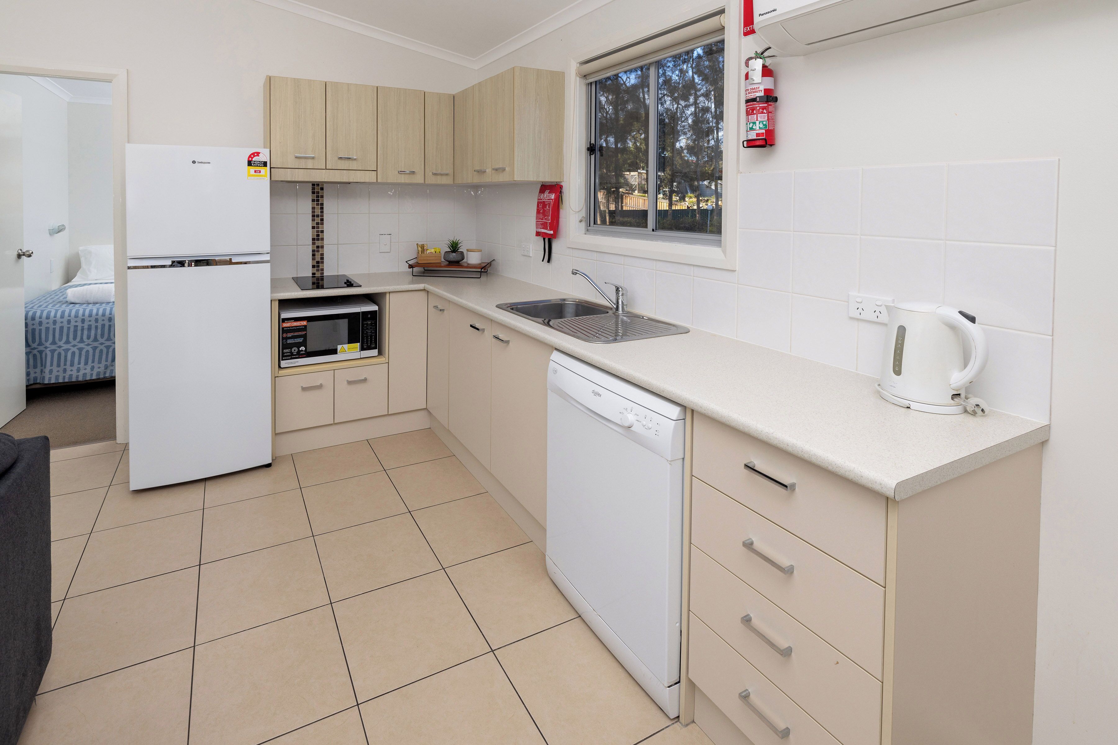 A compact kitchen with a dishwasher, a microwave, a sink, and a window with a view of the outdoors.