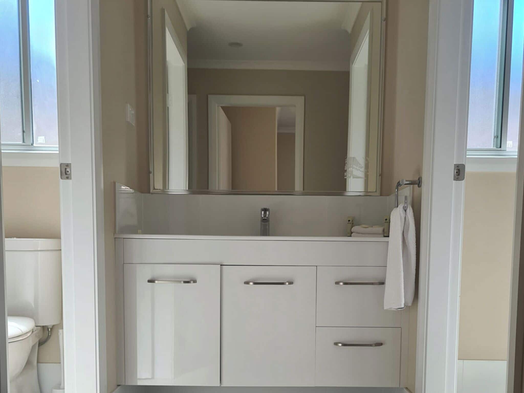 A bathroom with a white vanity, a mirror, and a towel hanging on the wall.