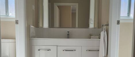 A bathroom with a white vanity, a mirror, and a towel hanging on the wall.