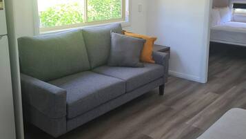 Un sofá gris con cojines en una habitación con suelo de madera y una ventana con vistas a la vegetación.