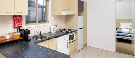 A compact kitchen with a gas stove, sink, and a microwave. There is a window above the sink, and a fire blanket is visible on the wall.